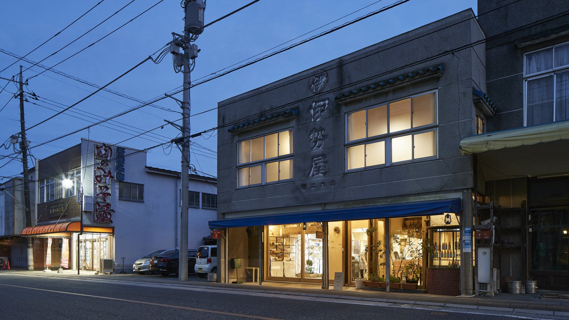 夕暮れの寄居町の商店街に建つmujaqui。築100年の建物の窓に灯りがともっている