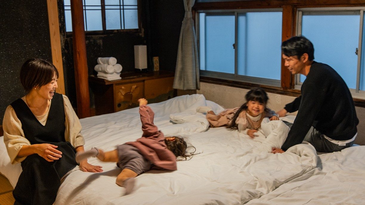 mujaquiの客室で、布団の上ではしゃぐ子どもと家族